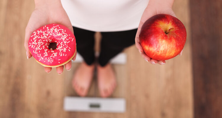 Kobieta na diecie stoi na wdze trzymając jabłko i pączka