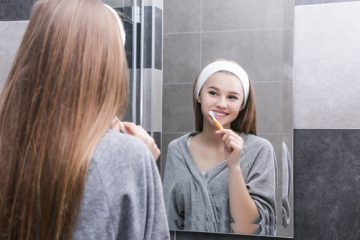 Młoda kobieta myjąca zęby przed lustrem w łazience
